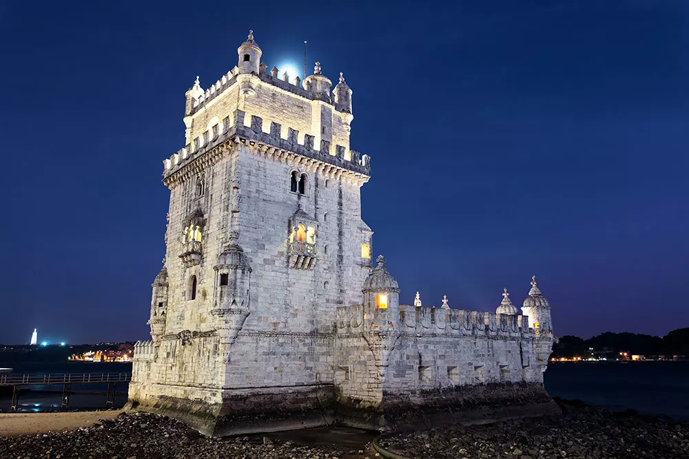 Fotografia noturna da Torre de Belém em Lisboa, Portugal, iluminada e refletindo seu icônico design histórico.